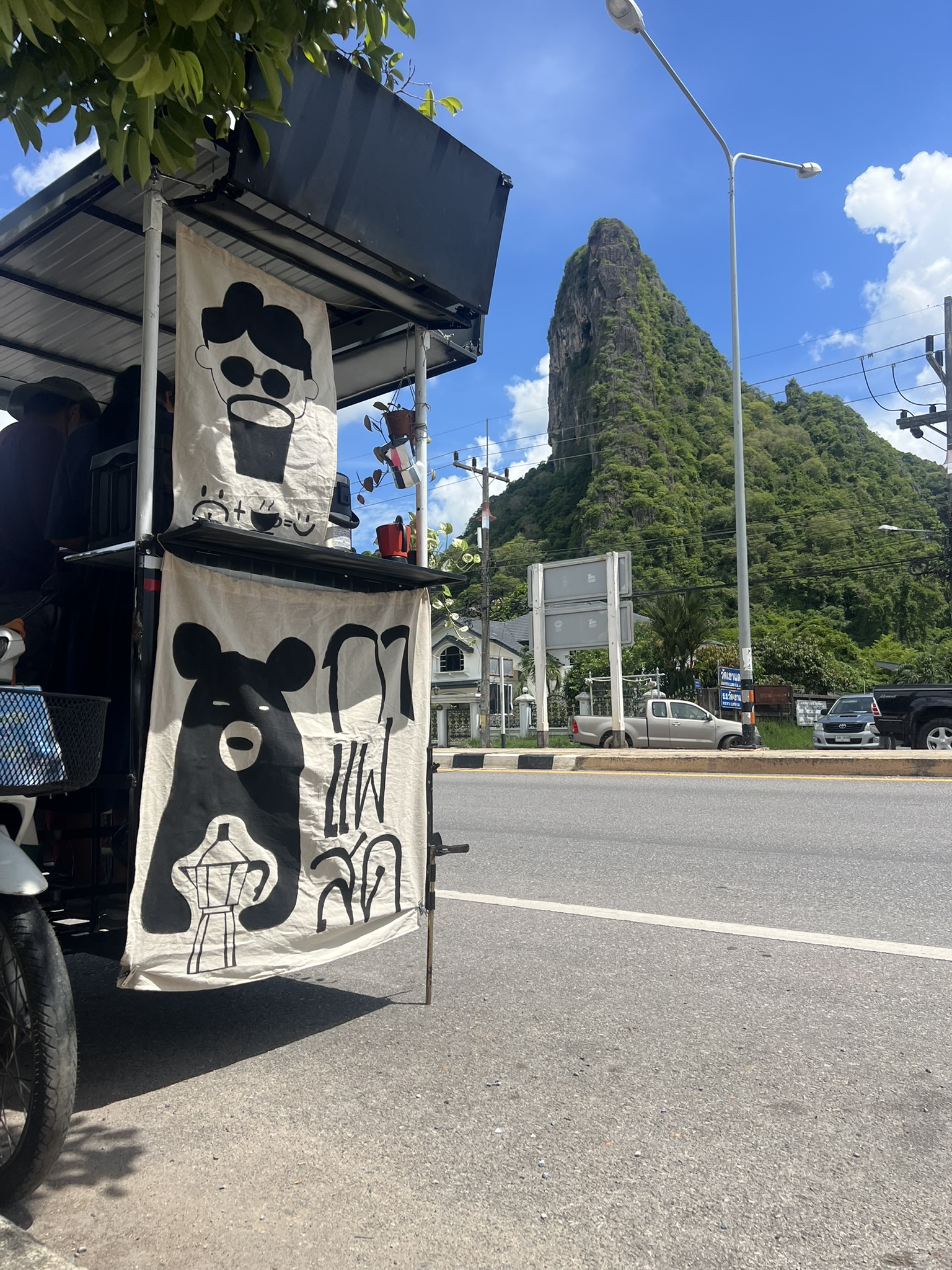 A small coffee cart beside the road with Khao Ok Thalu beyond