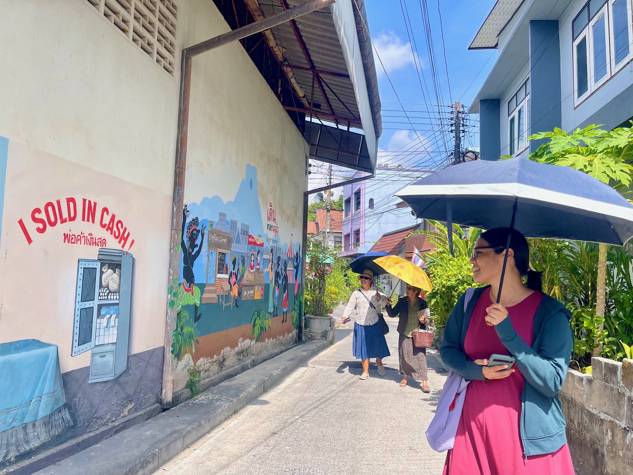Friends walking beside a colorful neighborhood mural in Phatthalung