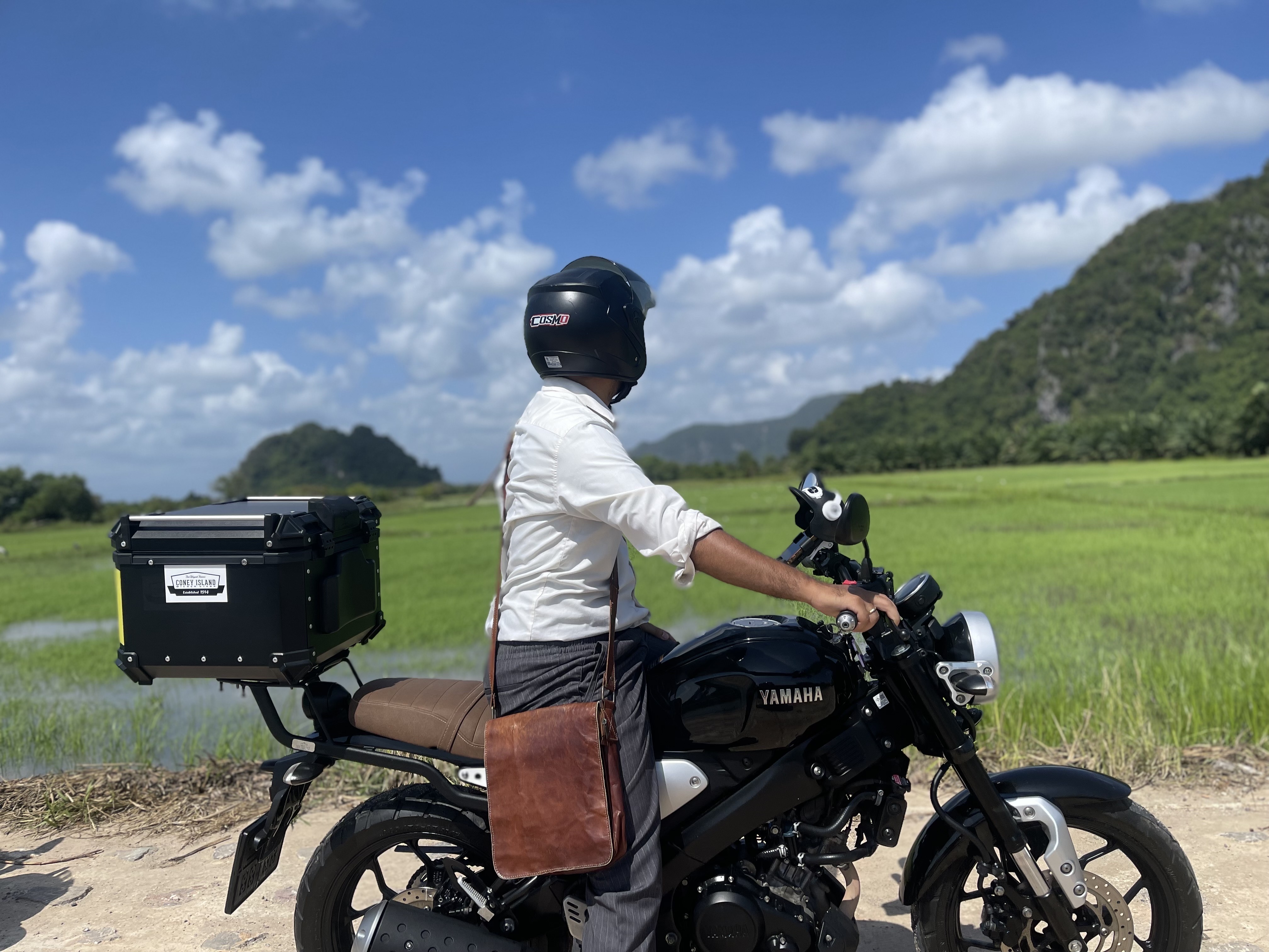 A motorbike rider pausing beside green rice fields and limestone hills