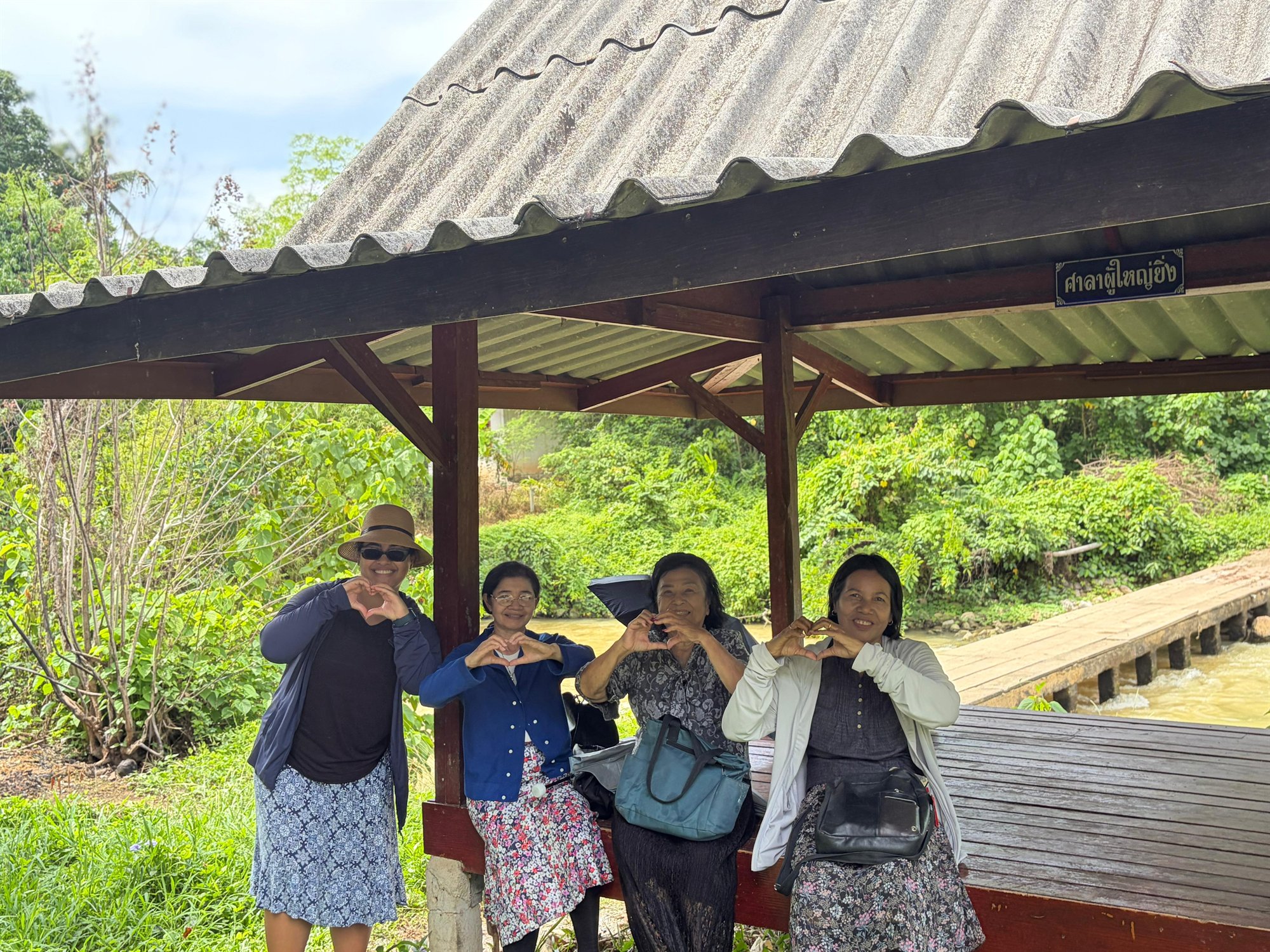 Four congregation friends making heart shapes together beside a forest stream