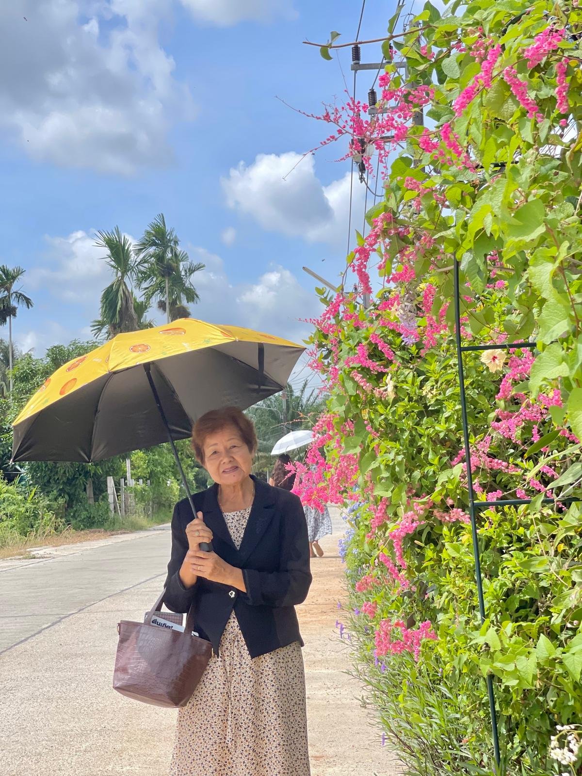 A congregation friend standing beneath an umbrella beside bright pink flowers