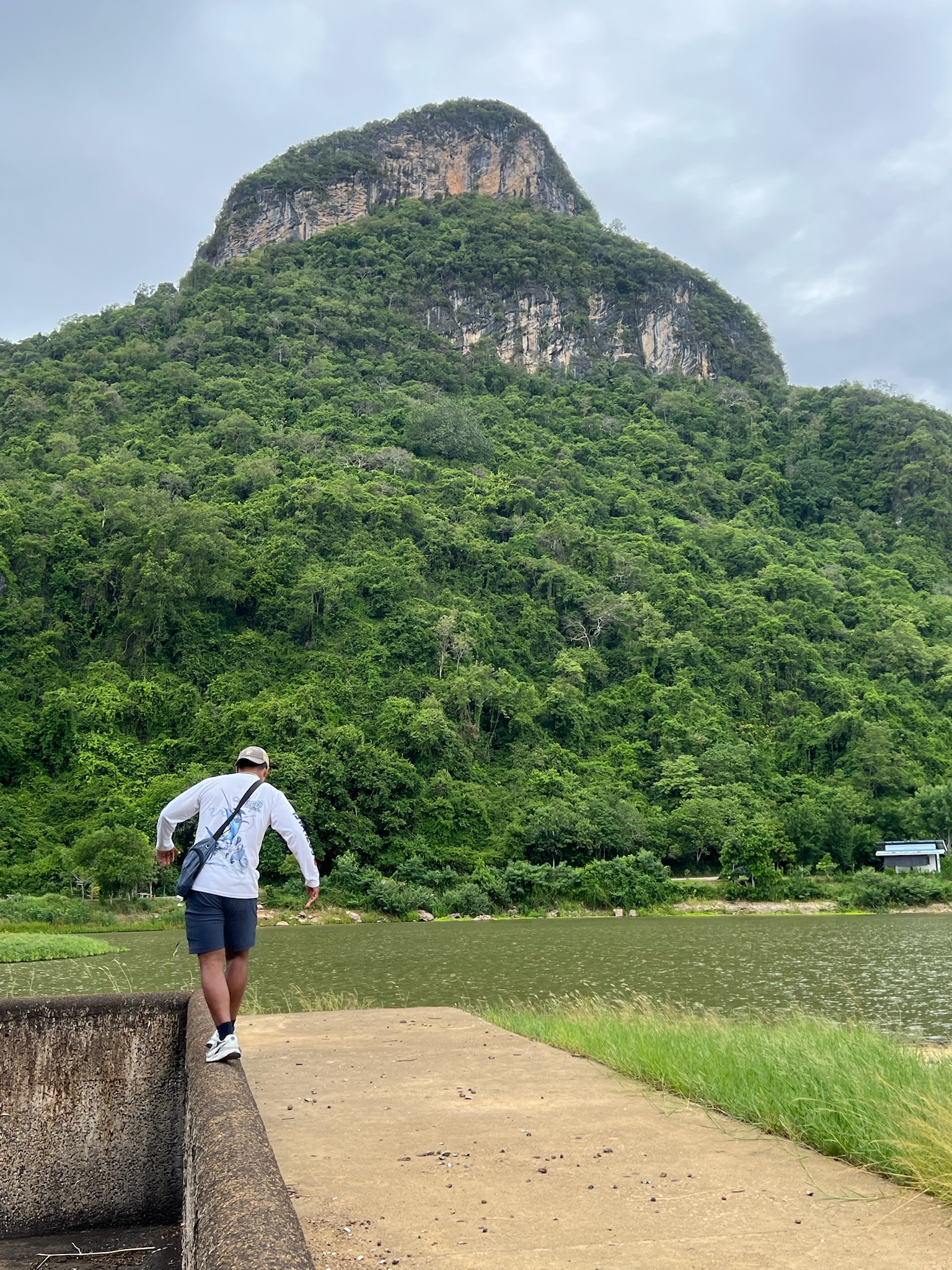 A friend walking beside a lake beneath a forested limestone mountain